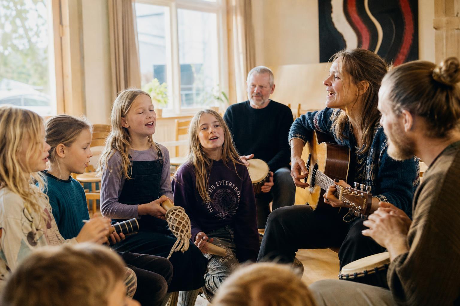 Børn og voksne i en musikkreds med guitar, trommer og rytmeinstrumenter